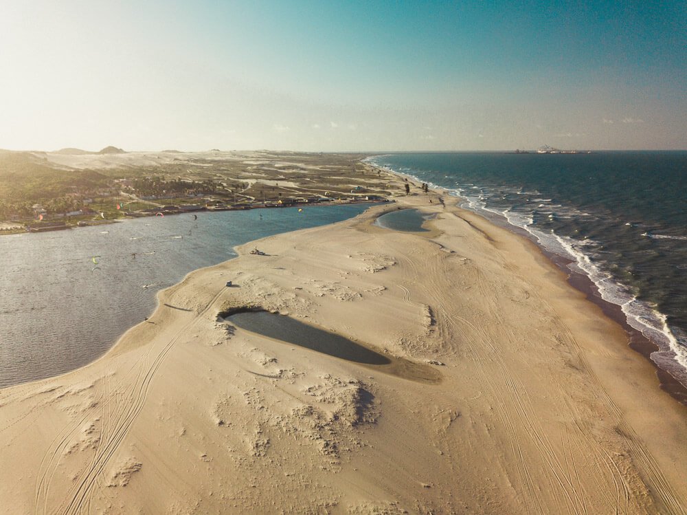 Foto aérea da lagoa Barra do Cauípe com praticantes de kitesurfe e o mar ao lado esquerdo