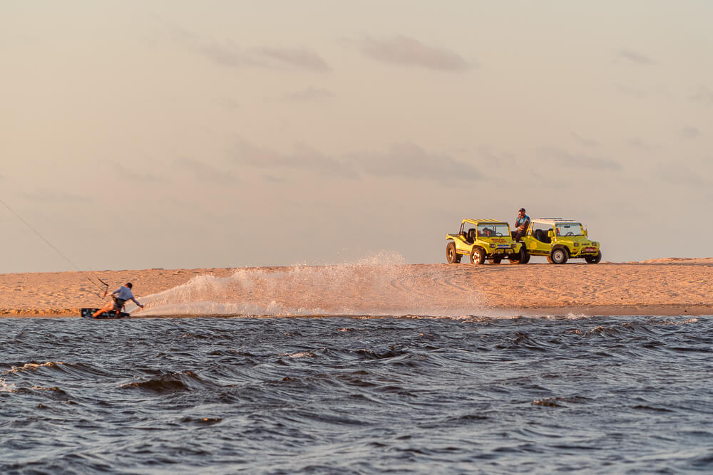 Dois buggys amarelos estacionados enquanto o motorista assiste a um praticante de kitesurf