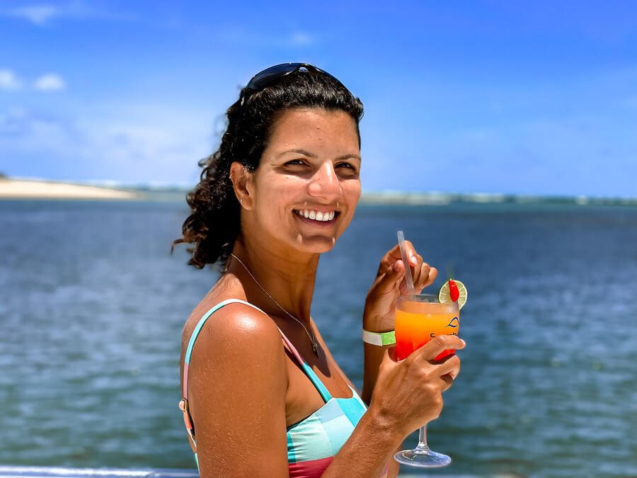 Mulher segurando um copo de drink e ao fundo o rio de Barra do Cunhaú