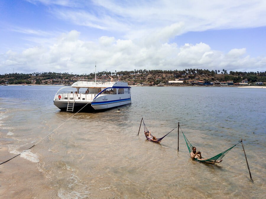 Rio em Barra do Cunhaú com um barco atracado e um casal deitados em redes sobre a água