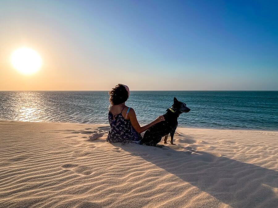 Mulher e cachorro sentados na Duna do Pôr do Sol em Jericoacoara observando o pôr do sol sobre o sol