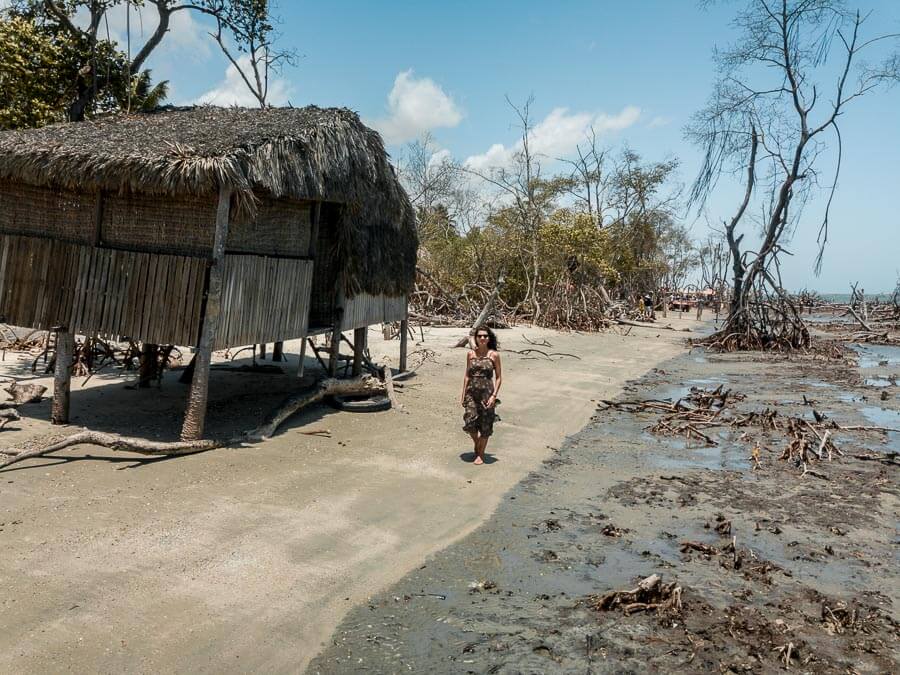 Mulher caminhando no na praia do Guriu onde há mangues e casinhas de palha
