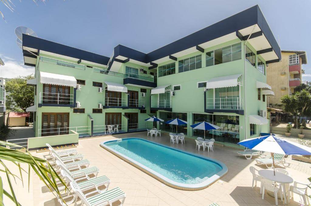 Piscina ao ar livre com espreguiçadeiras, mesas e guarda-sóis em pousada de três andares