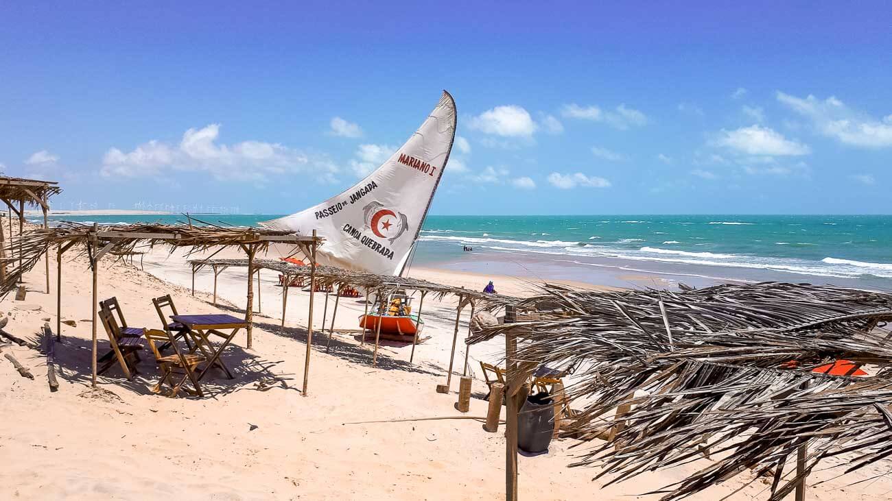 Areia da Praia de Canoa Quebrada com uma jangada e barracas de palhas