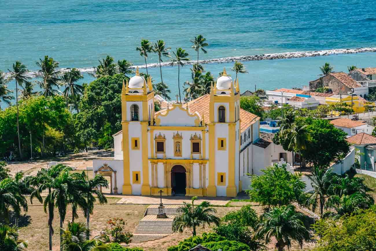 Igreja do Carmo em Olinda com arquitetura colonial e duas torres laterais. Ao fundo o mar.
