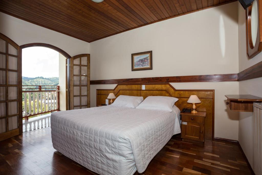 Quarto de casal com piso e teto de madeiras e sacada com vista para natureza.