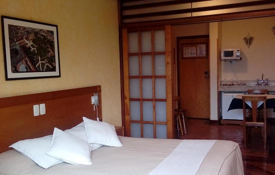 Quarto de casal com móveis de madeira e ao fundo uma cozinha