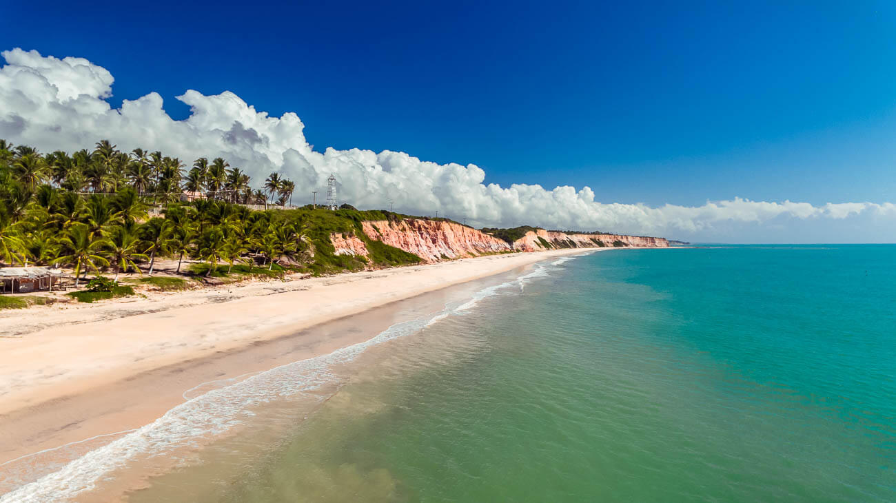 Vista panorâmica do mar em tons azuis esverdeados da Praia do Farol em Prado e ao fundo falésias com vegetação