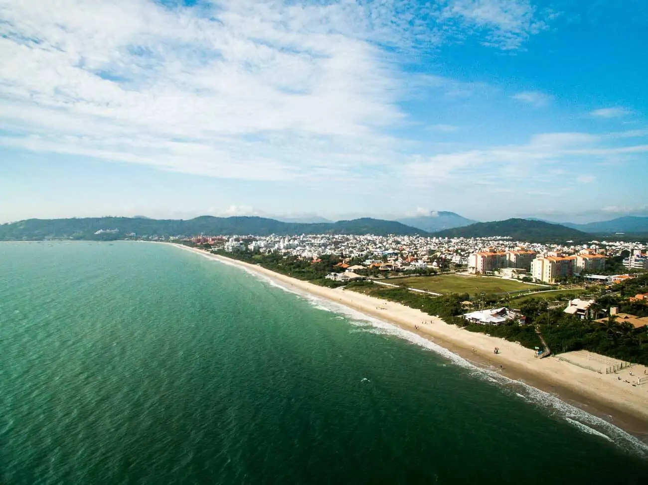 Vista panorâmica de uma parte da Praia de Jurere com vegetação na orla e ao fundo construções.