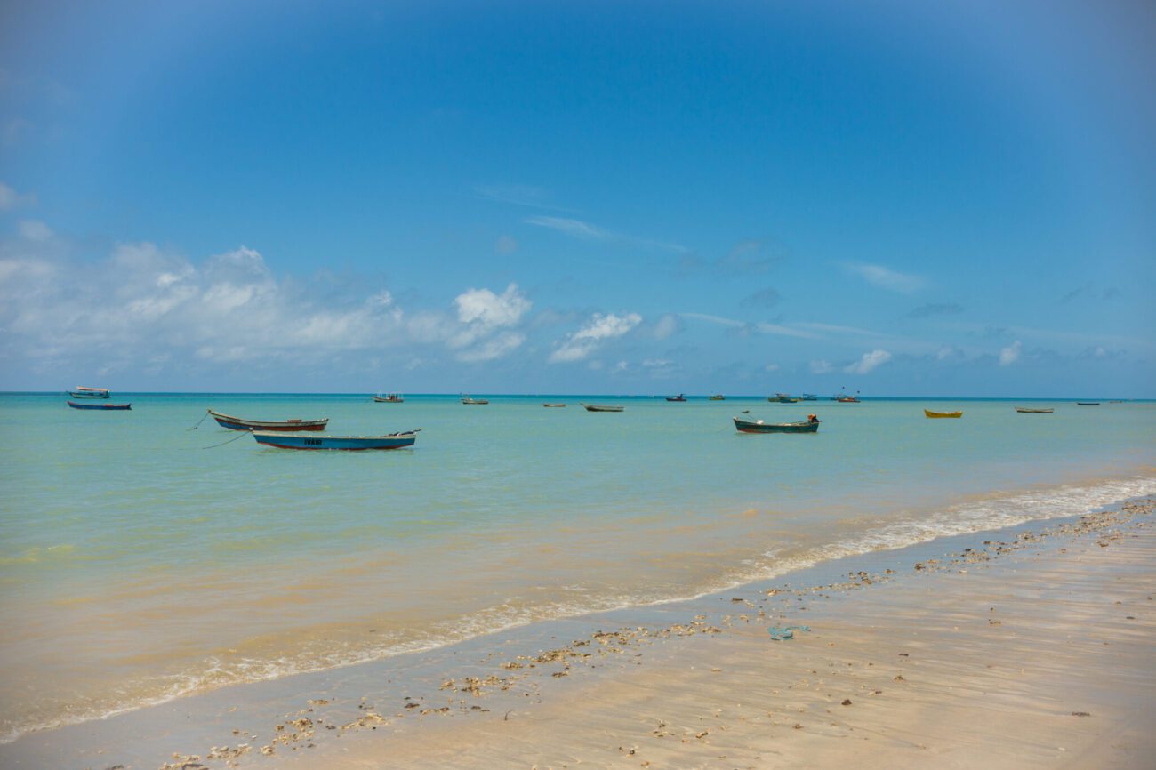 Barcos em mar de águas cristalinas e sem ondas da Praia de Cumuruxatiba.