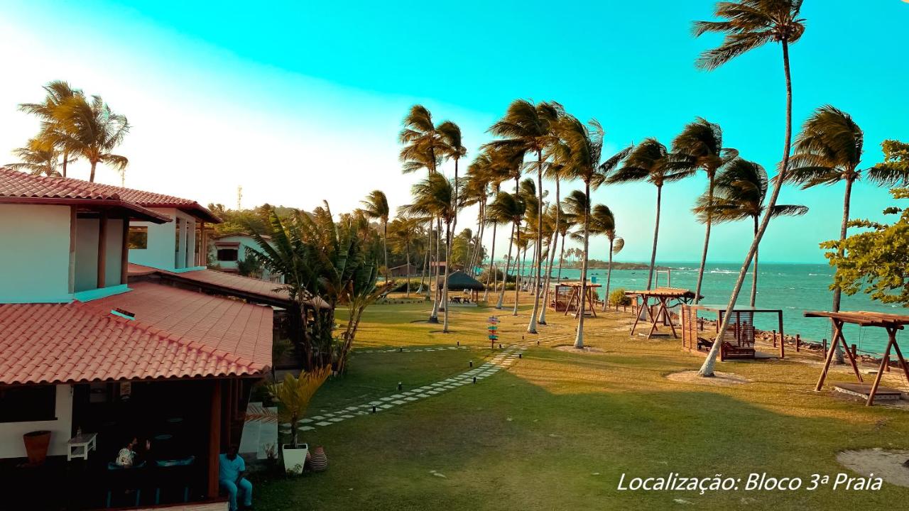 Área gramada com alguns coqueiros e decks com espreguiçadeiras, cadeiras e sofás com vista para a Terceira Praia.