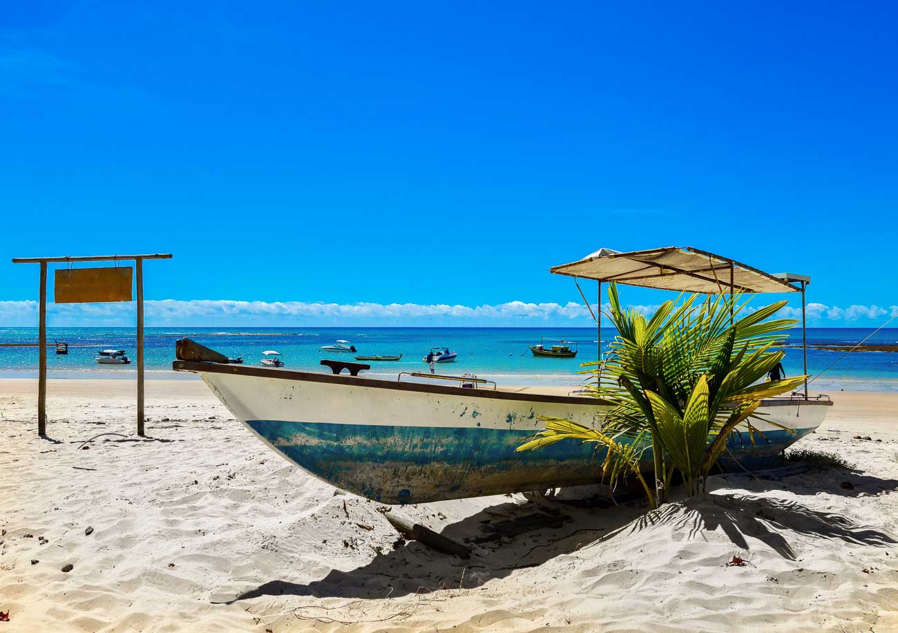 Barco na areia em Praia em Trancoso com o mar azul ao fundo.