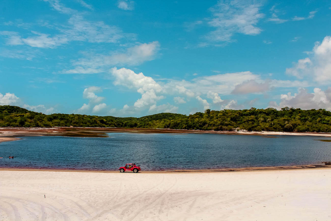 Lagoa da Coca-Cola com águas escuras e um buggy vermelho parado na areia.