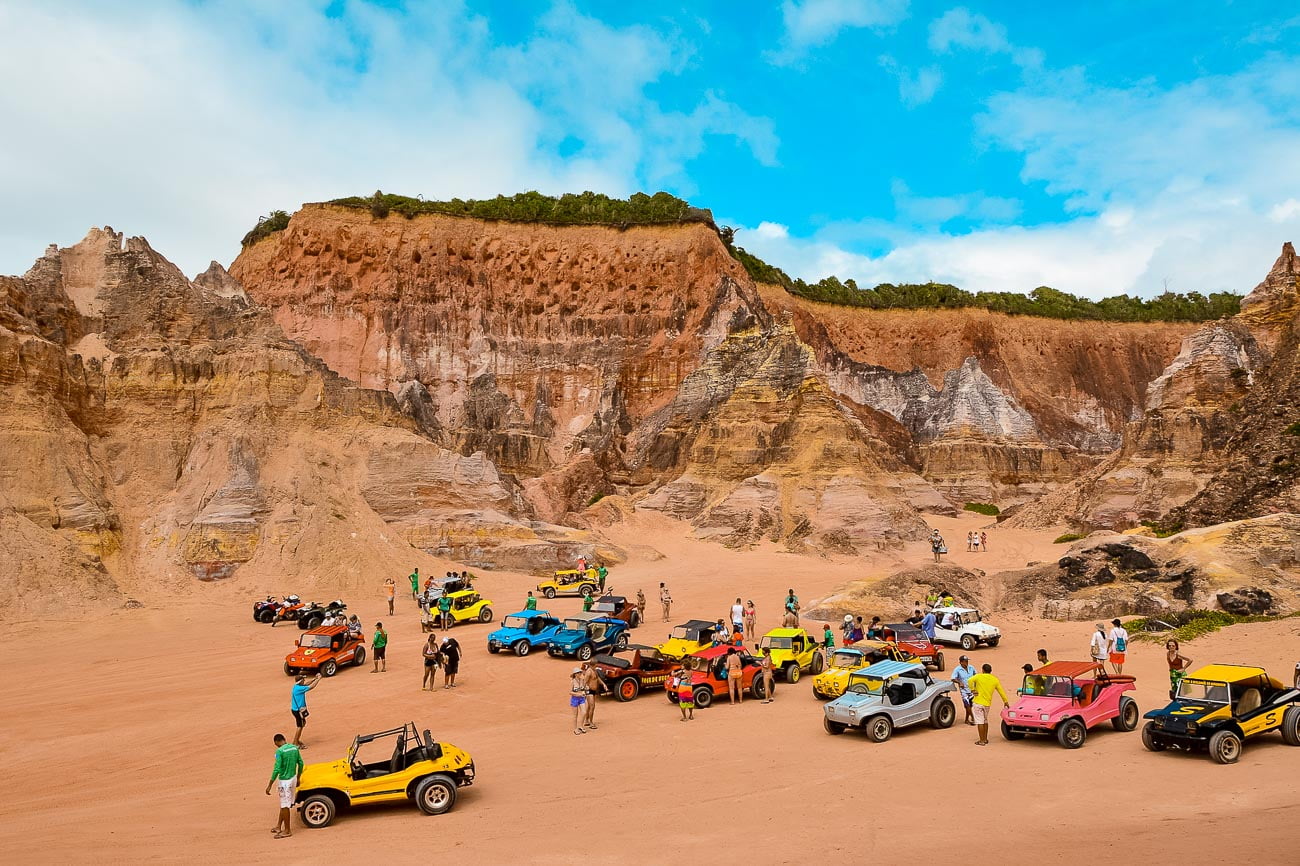 Vários buggys de diferentes cores parados na falésias da Praia do Gunga com turistas