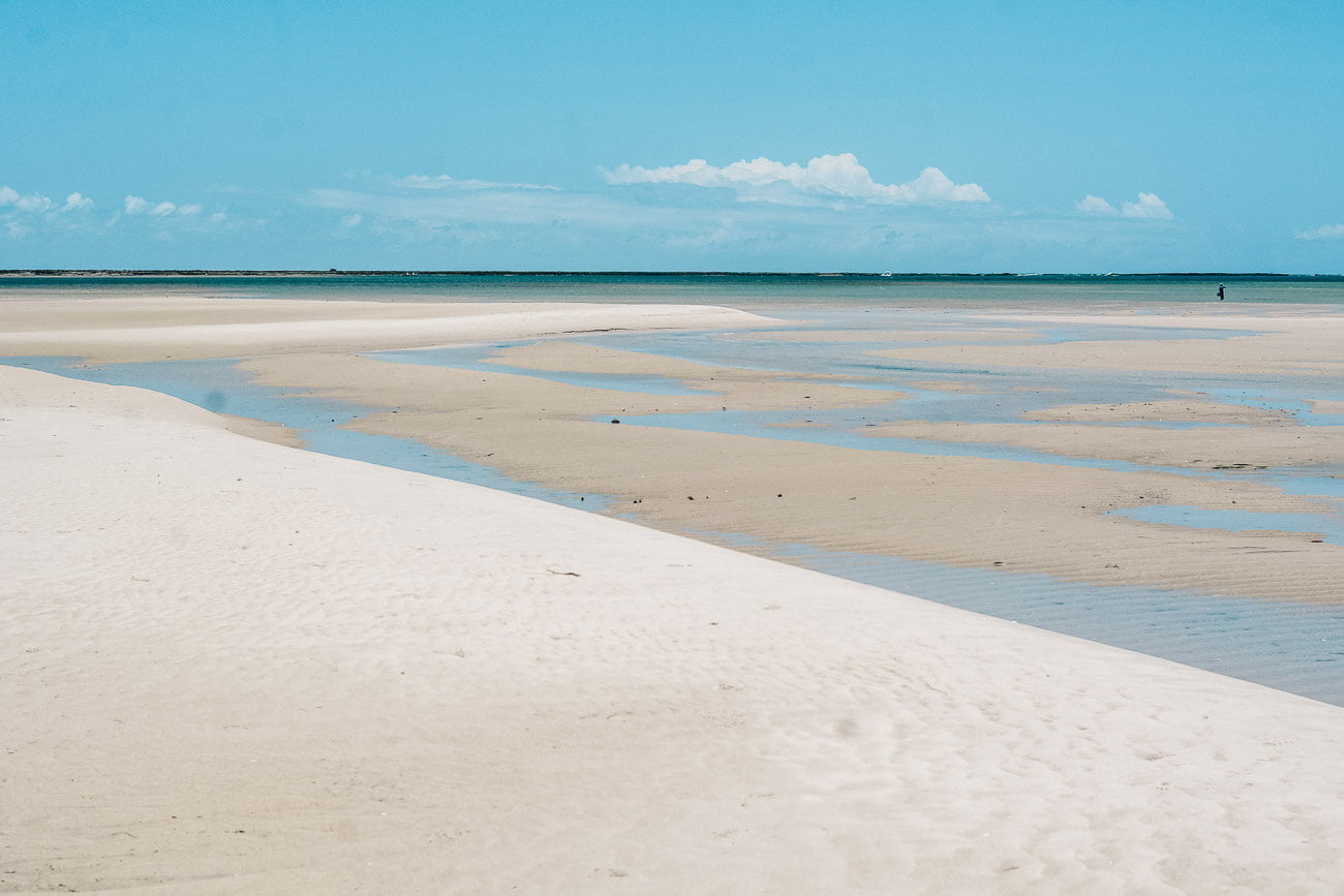 Faixa de areia branca e ao fundo o mar calmo e cristalino da Praia das Conchas