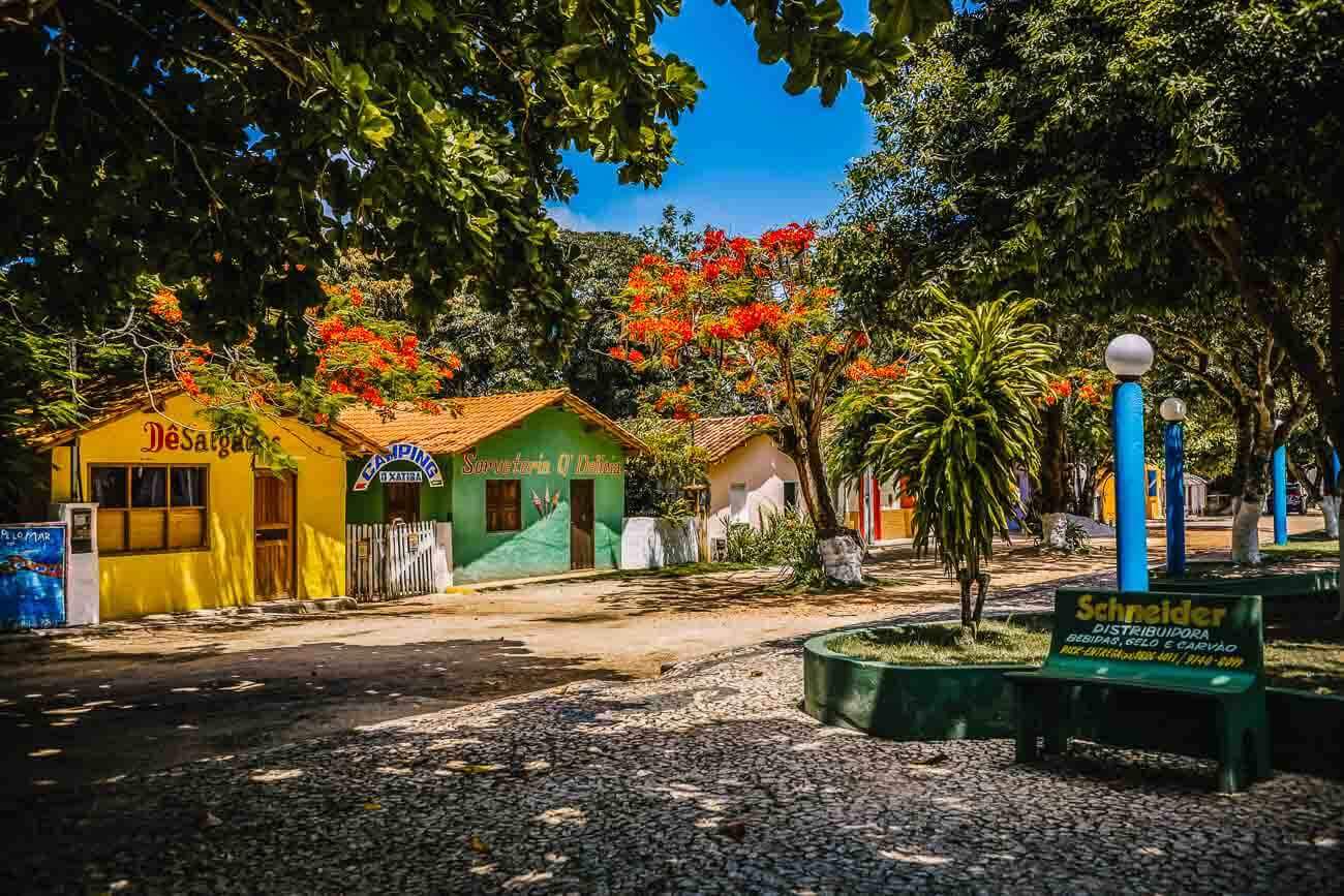 Casinhas coloridas e uma pequena pracinha com árvores e um banco em Cumuruxatiba