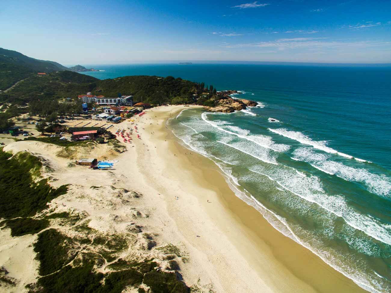 Vista de cima da Praia da Joaquina em Florianópolis. Há uma concentração de barracas na parte do costão.