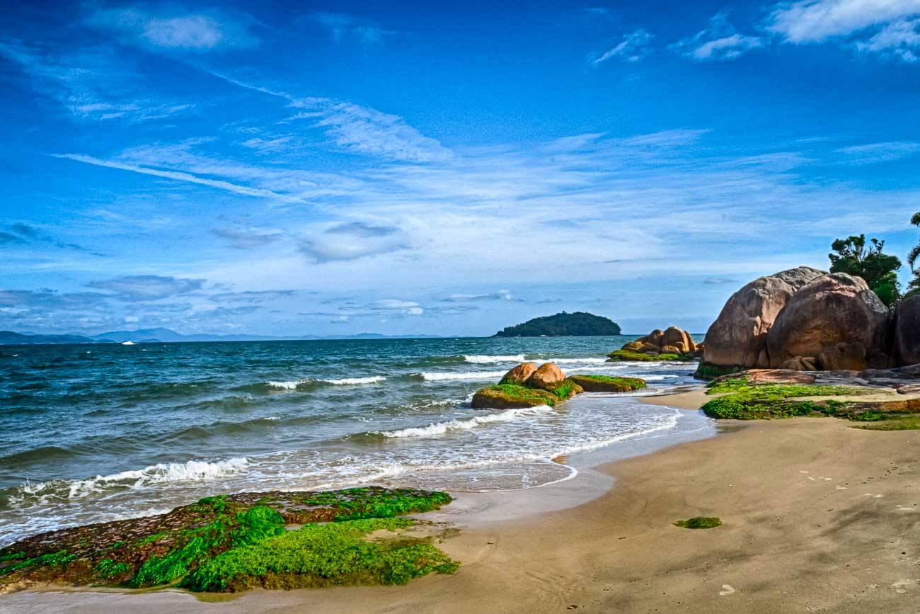 Praia de Jurerê com o mar calmo e algumas pedras na areia
