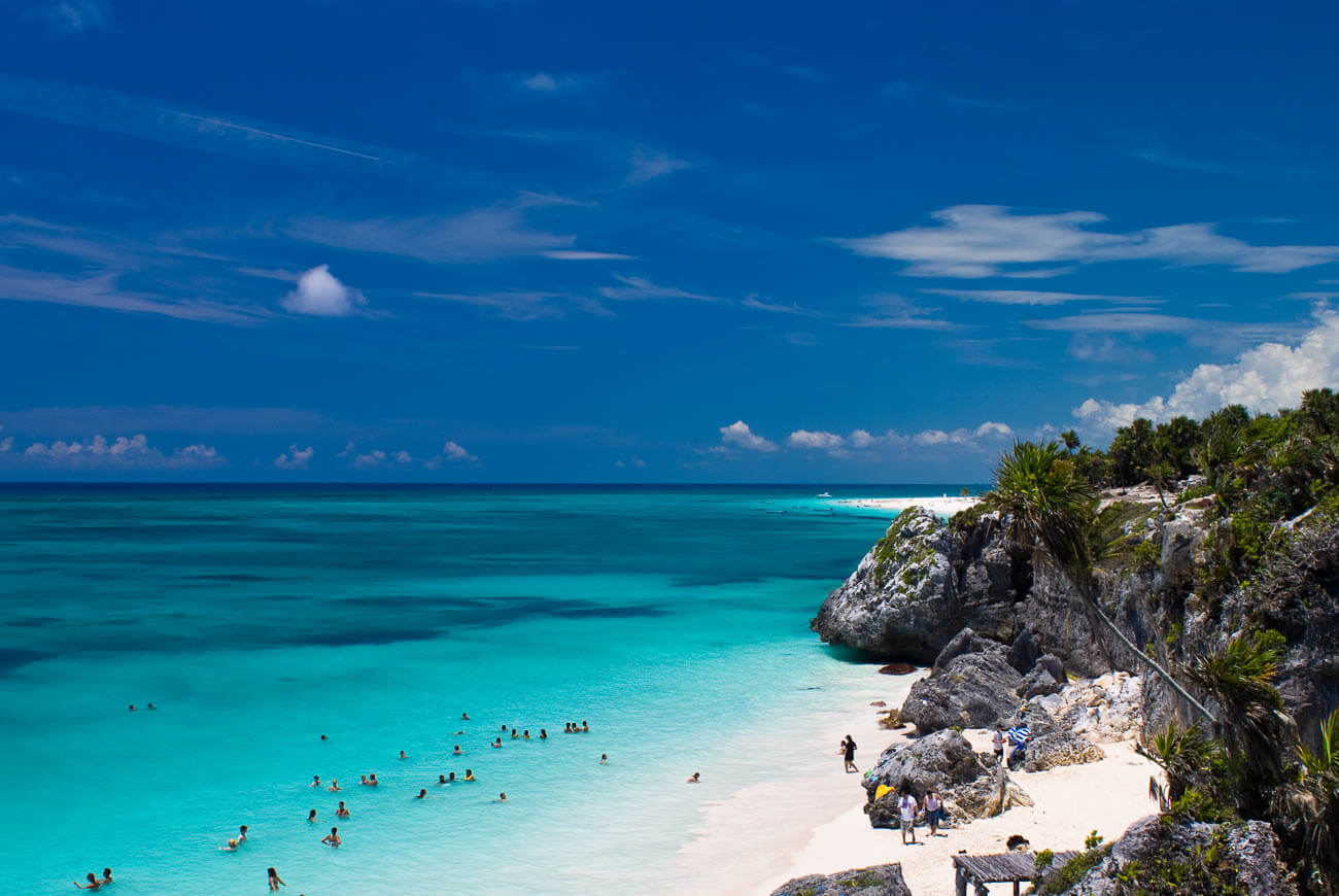 Vista do alto de praia em Tulum com o mar em tom de azul turquesa com alguns banhistas.