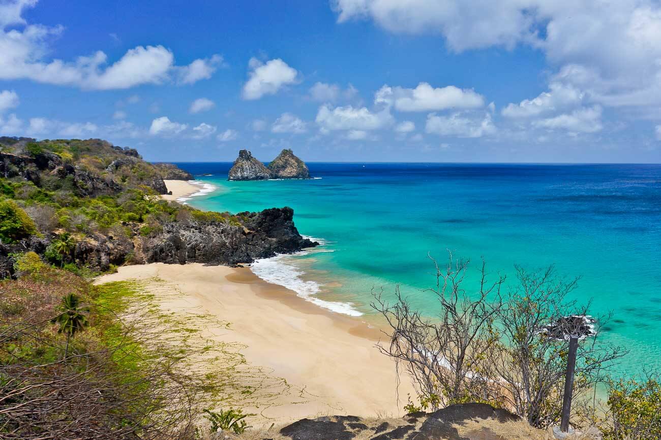 Vista do Mirante do Boldró para a praia com areia vazia e o mar cristalino em tons azuis.