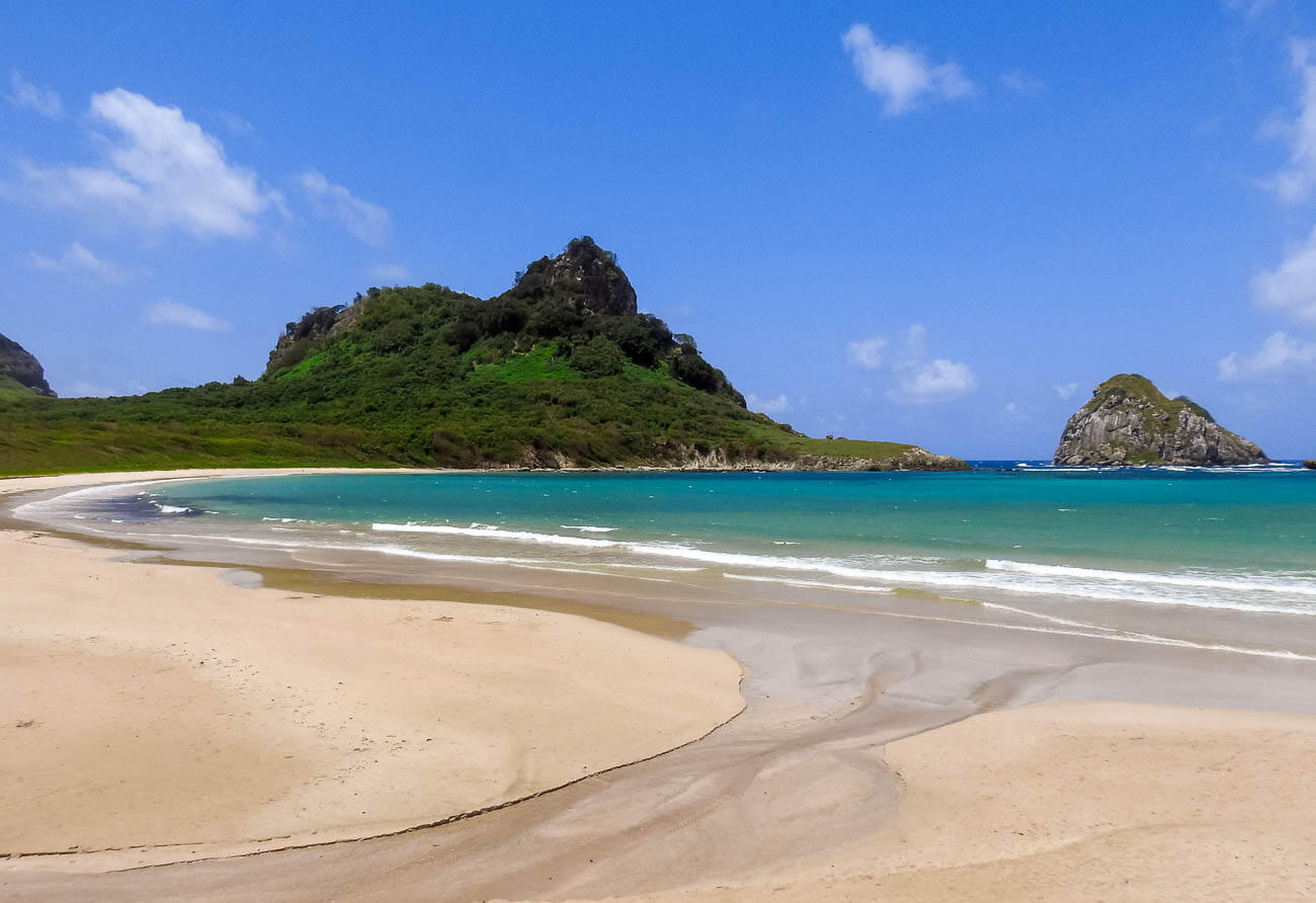 Praia da Conceição com o mar azul turquesa com ondas baixinhas, cercada por natureza.