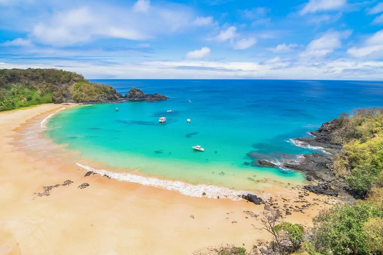 Praia do Sancho com a faixa de areia vazia e o mar cristalino em tom turquesa com alguns barcos.