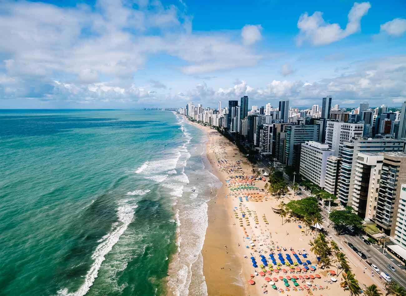 Vista de cima e panorâmica de uma parte da Praia de Boa Viagem em Recife com o mar em tons de azuis esverdeados.