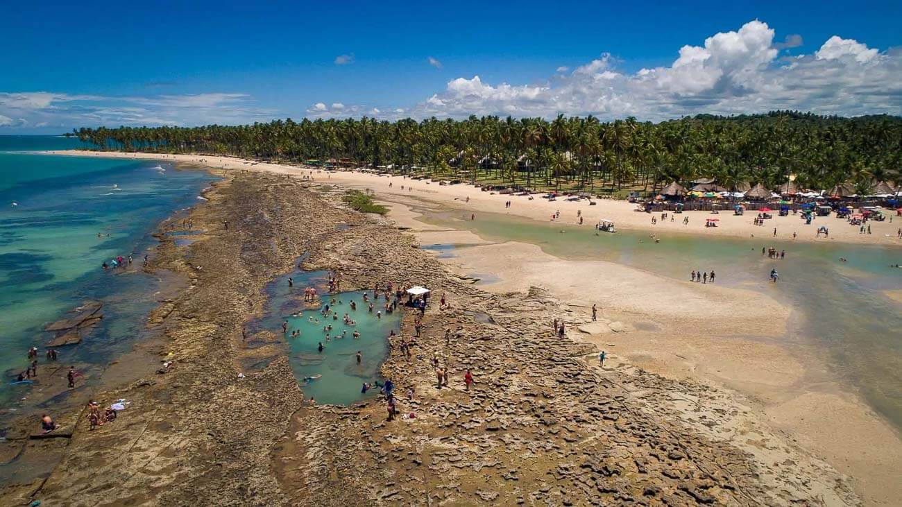 Vista panorâmica das piscinas naturais na Praia dos Carneiros com banhistas.