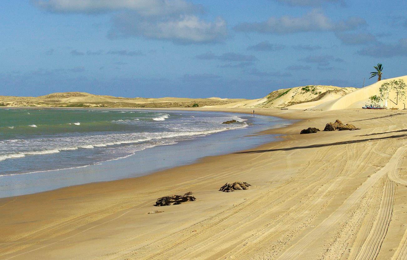Faixa de areia larga e extensa na Praia de Maracajaú, cercada por dunas.