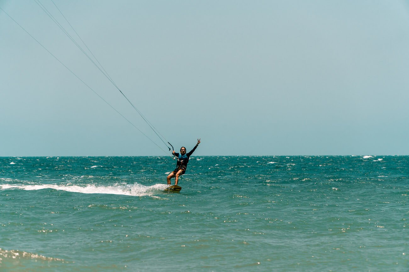 Um homem praticando kitesurfe no mar azul esverdeado da Praia do Preá