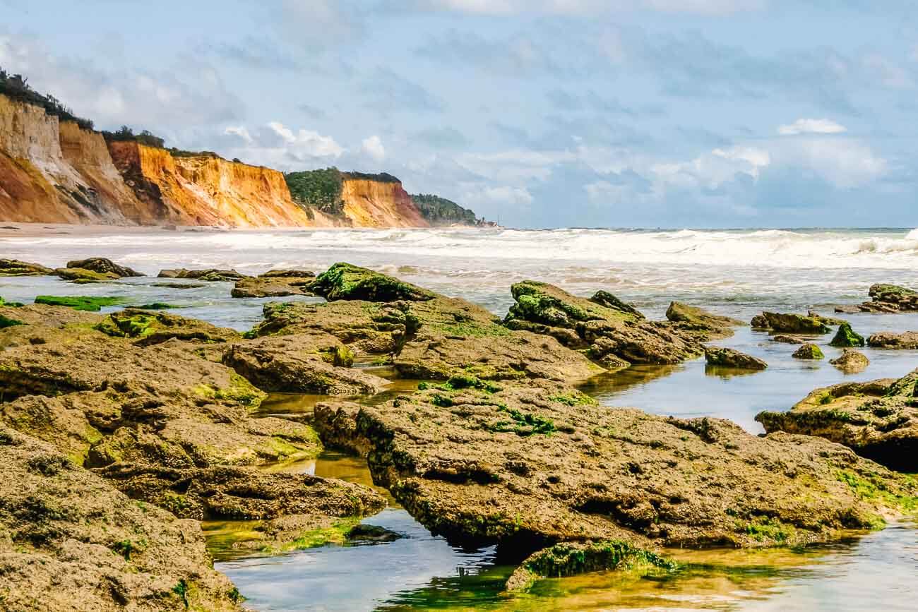 Pedras com lodo na Praia de Jacarecica do Su com o mar agitado com ondas fortes e falésias na orla.