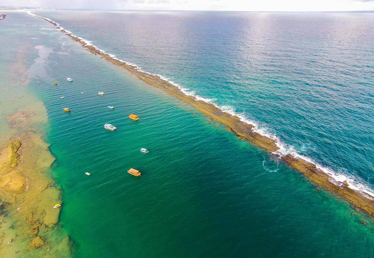 Vista de cima da barreira de corais na Praia do Francês, com o mar calmo de um lado e agitado do outro