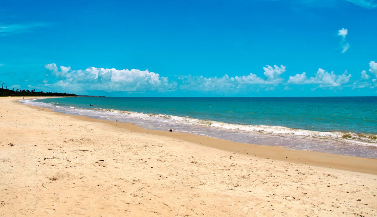 Faixa de areia larga e extensa na Praia de Corumbau Bahia, com o mar azul turquesa sem ondas.