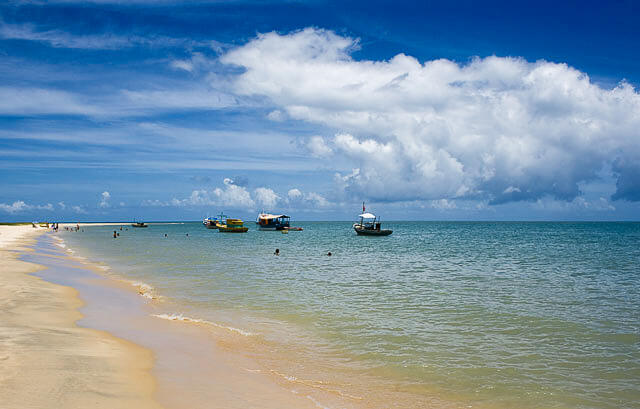 Embarcações na água na Ponta do Corumbau com o mar tranquilo com alguns banhistas.