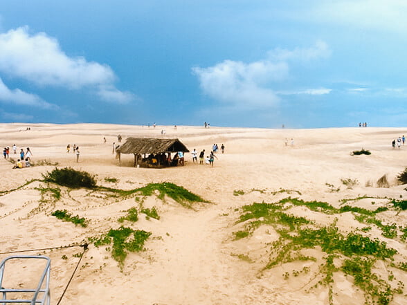 Dunas conhecidas como Morro Branco, com áreas com restinga e algumas pessoas caminhando.
