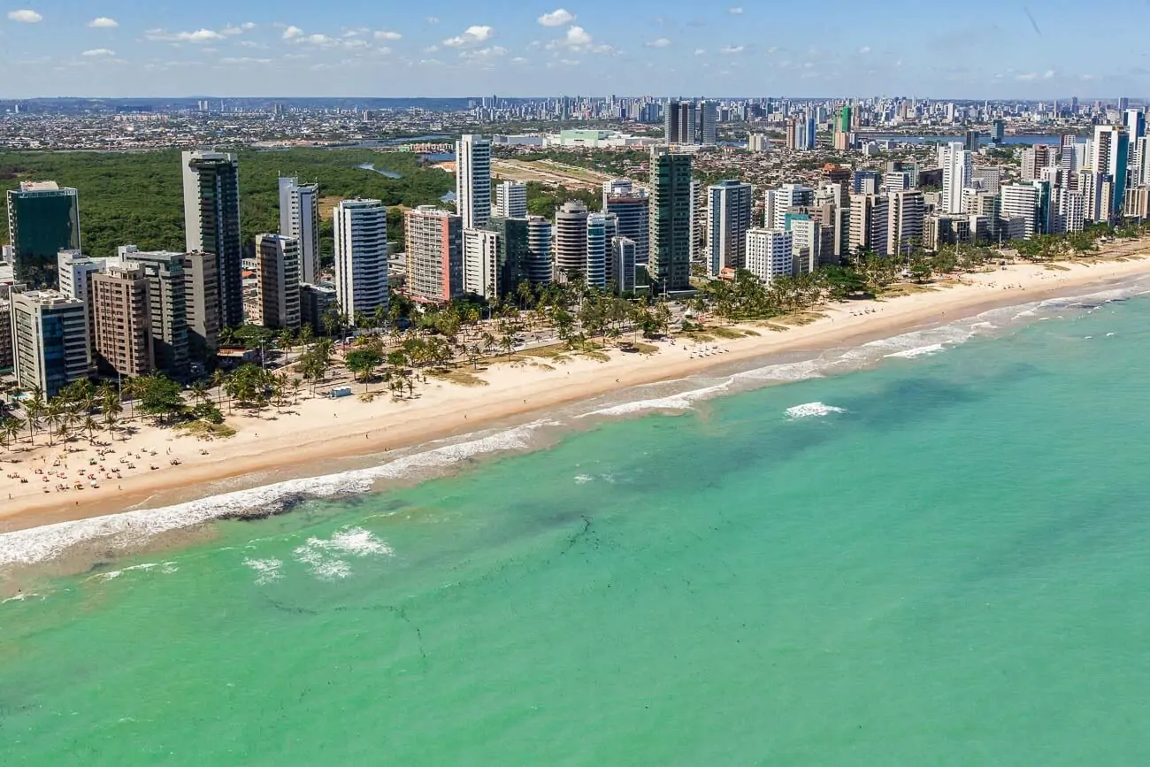 Vista aérea da Praia do Pina em Recife com o mar azul cristalino e prédios na orla.