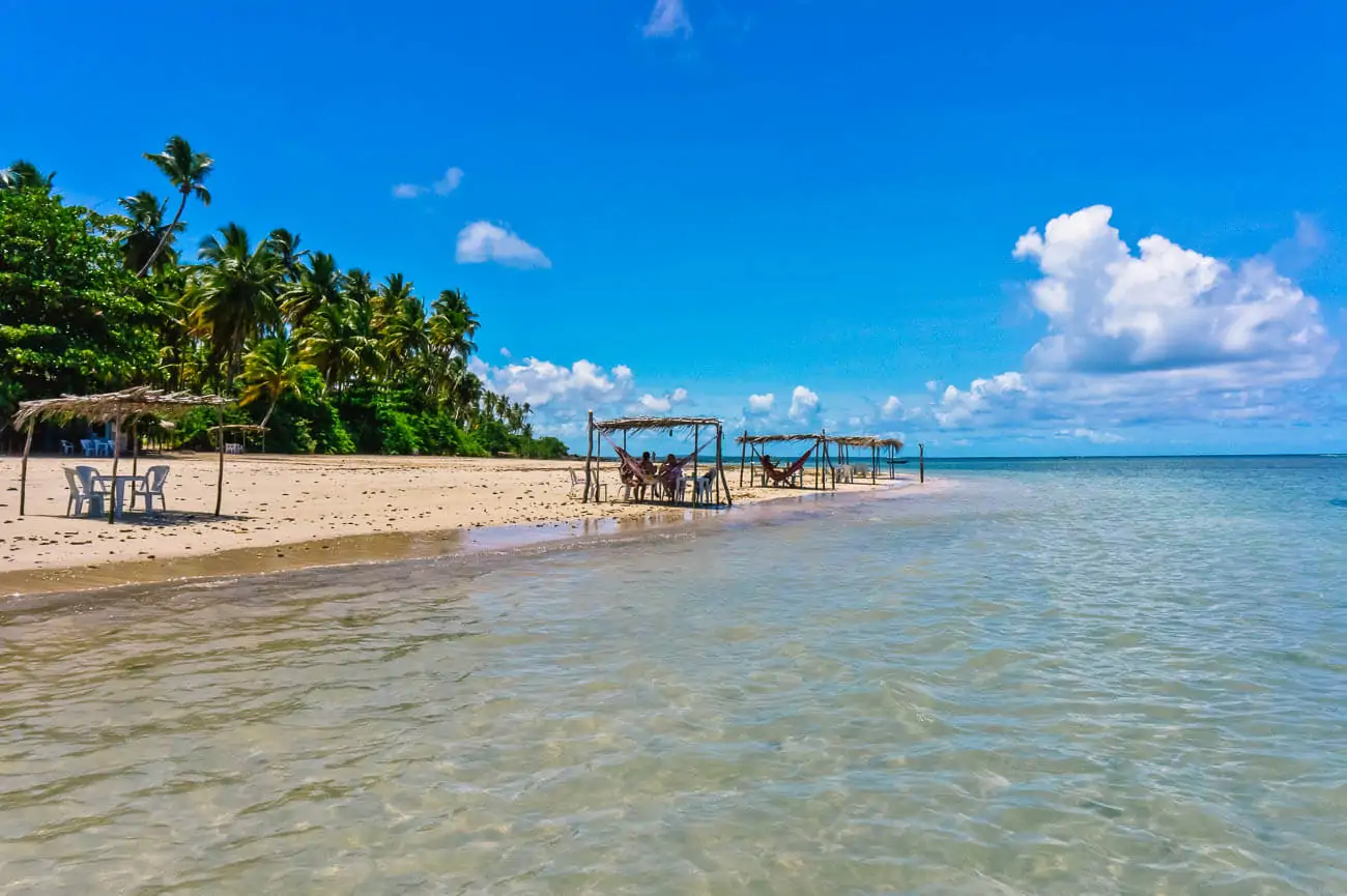 Praia na Ilha de Boipeba com algumas barracas de palha com redes, mesas se cadeiras.