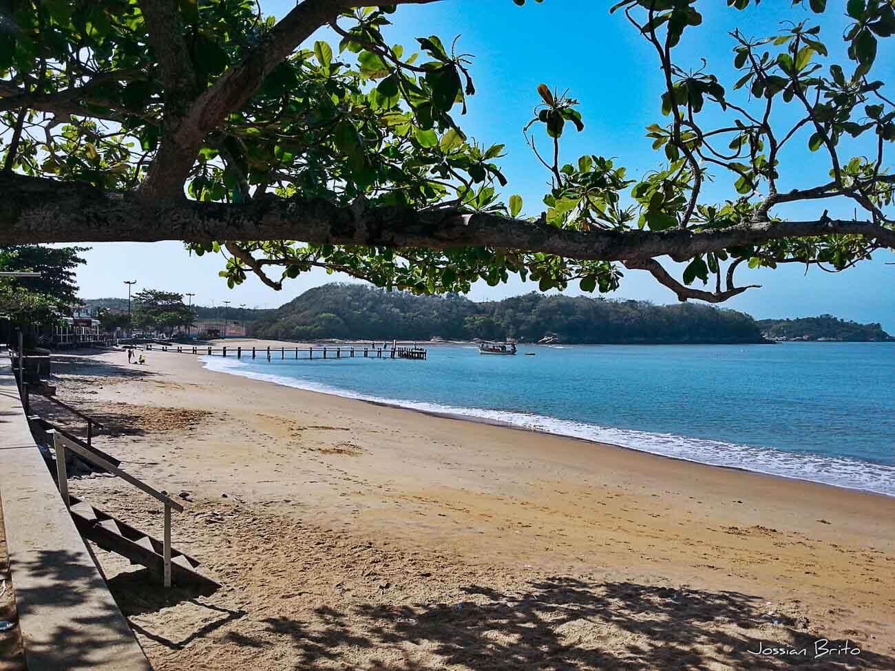 Faixa de areia vazia da Praia do Centro em Rio das Ostras e ao fundo um píer.