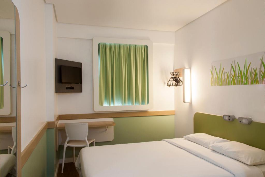 Quarto de casal pequeno em hotel em Manaus. Há uma bancada com cadeira e uma TV na parede.