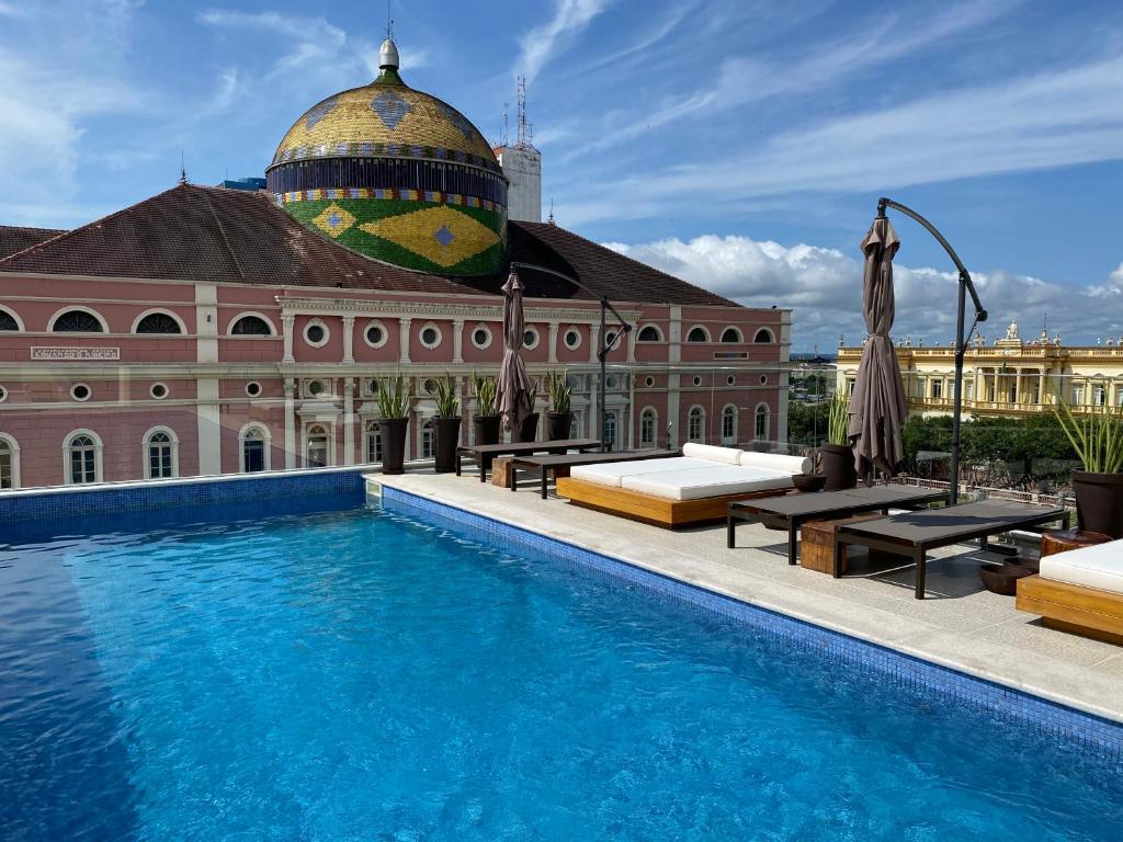 Piscina em terraço de hotel em Manaus com espreguiçadeiras e camas no estilo balinesas. Ao fundo, vista para o Teatro Amazonas.