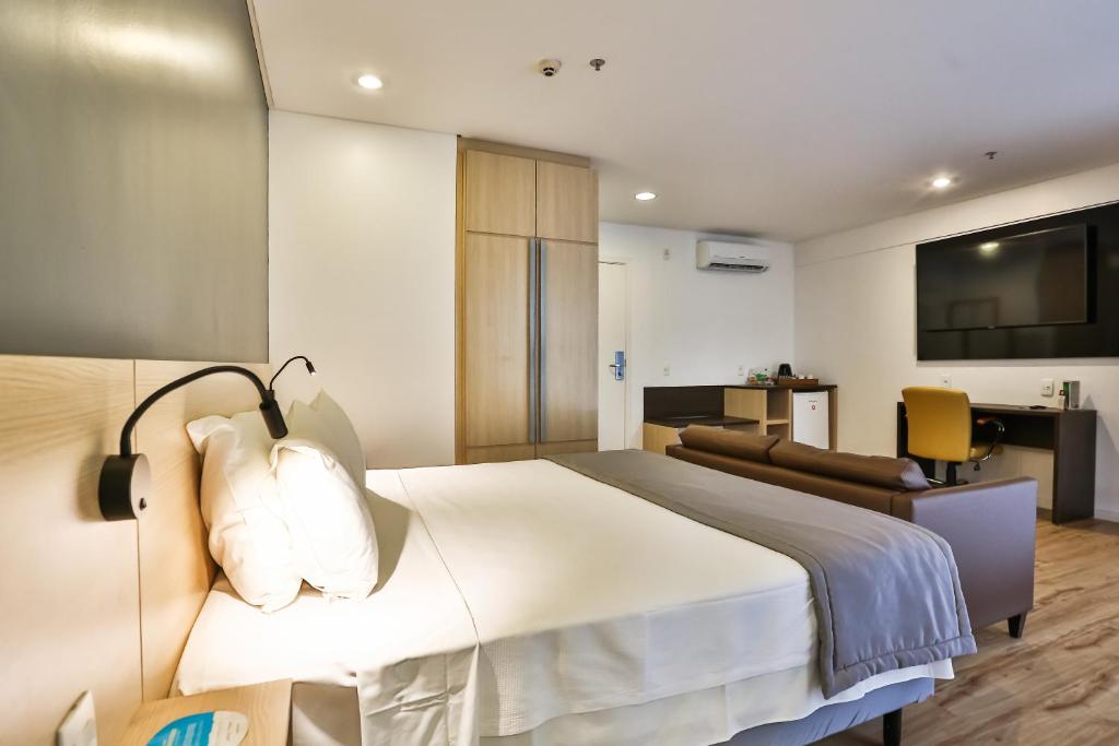 Quarto de casal com decoração moderna. Há um sofá, tv em um painel e roupeiro.