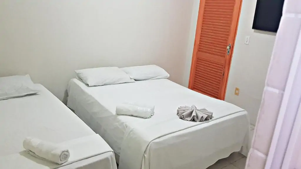 Quarto com camas de casal e cobre leito todo branco.