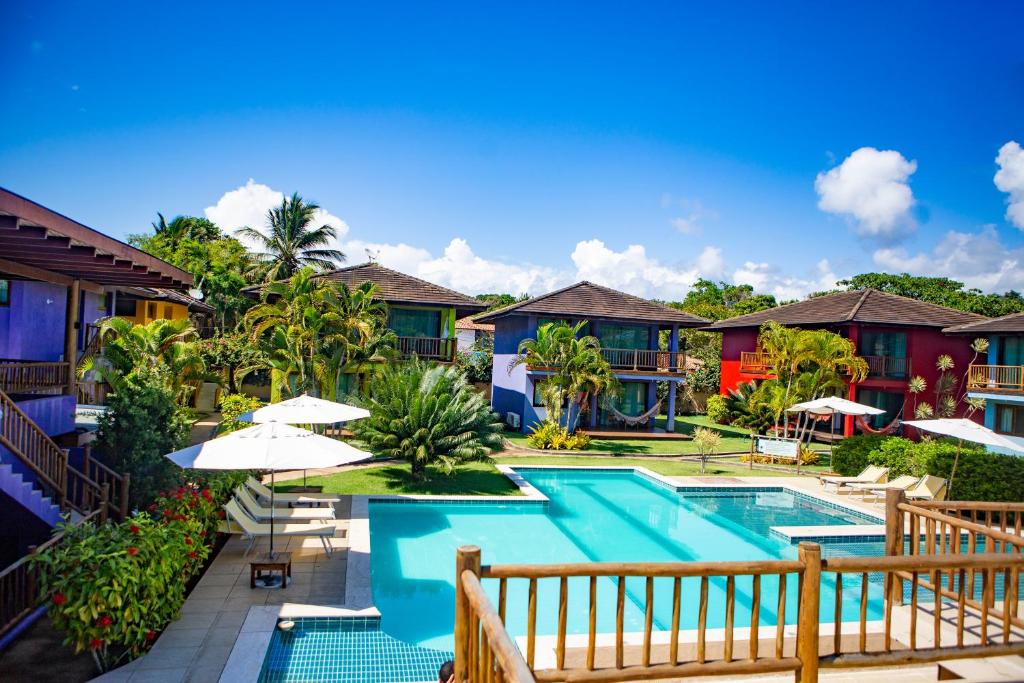 Piscina ao ar livre, cercada por área gramada, com flores e canteiros. Ao fundo, casas de dois andares coloridas.