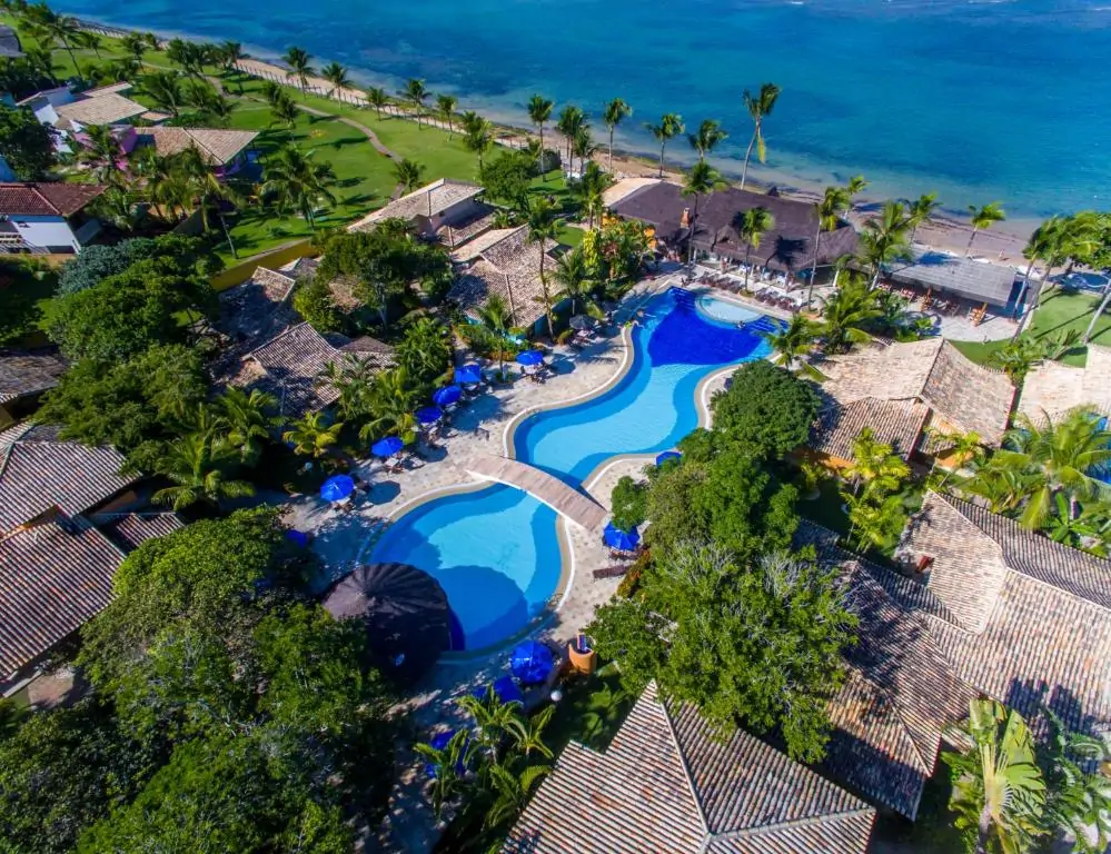Vista aérea de hotel com complexo de piscinas, cercado por natureza e ficando de frente para a Praia do Mucugê.