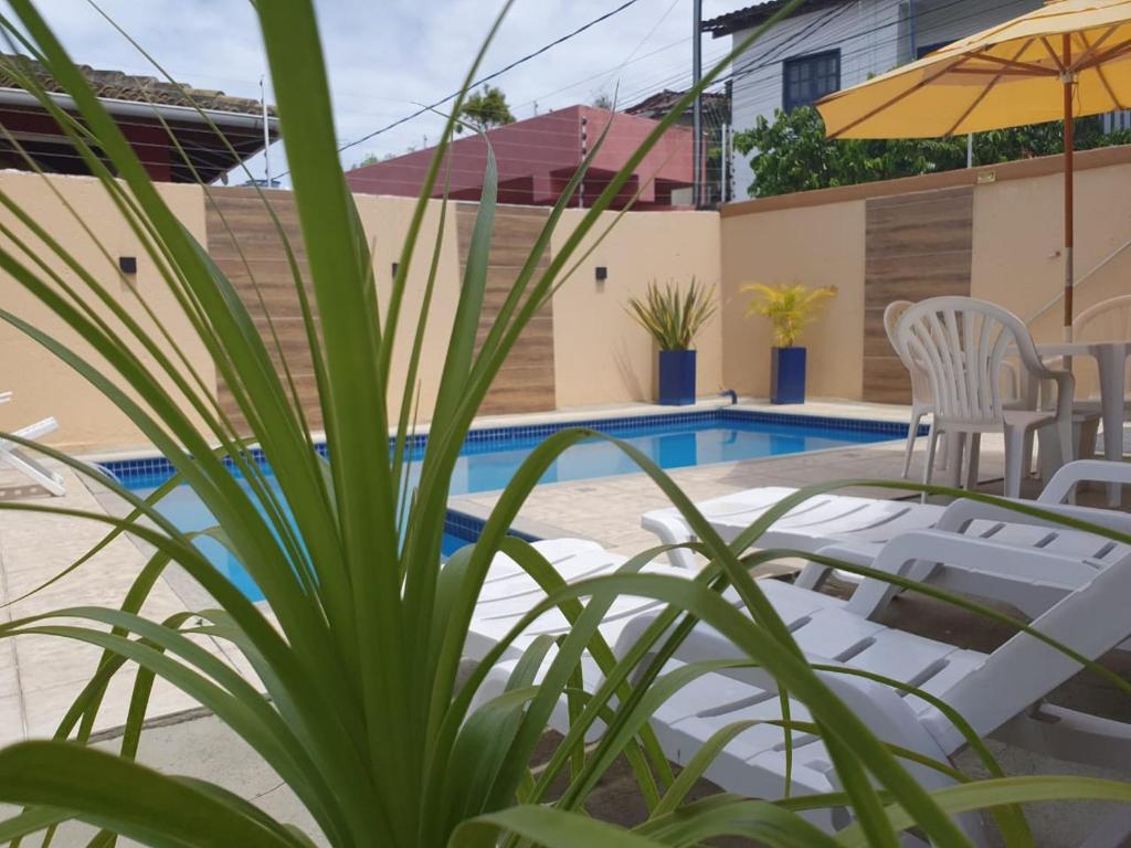 Piscina em área externa de pousada com mesas, cadeiras e espreguiçadeiras em volta.