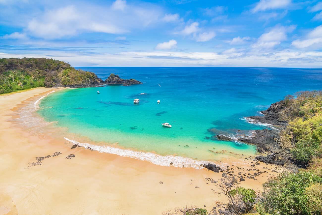 Praia do Sancho com a faixa de areia vazia e o mar cristalino em tom turquesa com alguns barcos.