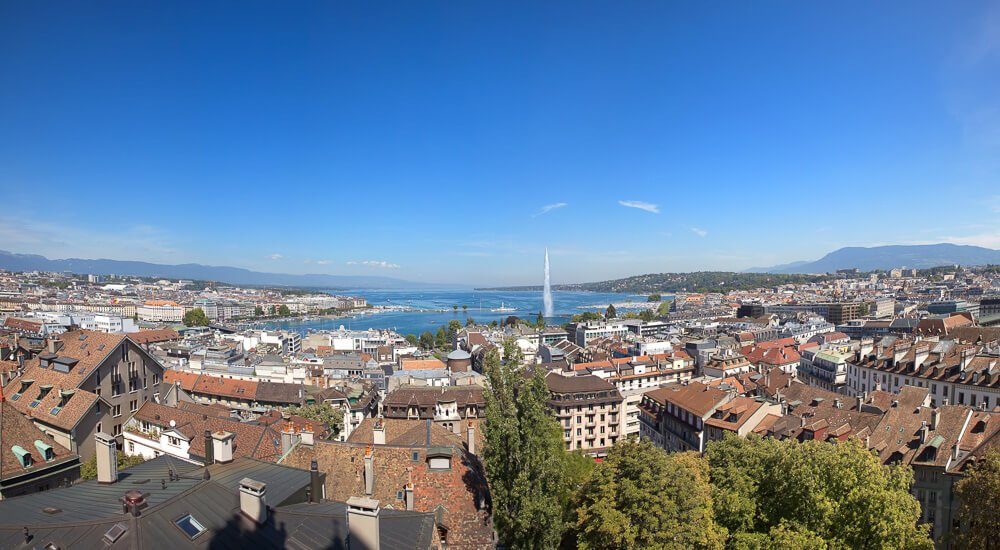 Vista superior da cidade de Genebra, na Suíça. Há muitos edifícios tradicionais e históricos cercando um lago na região central.