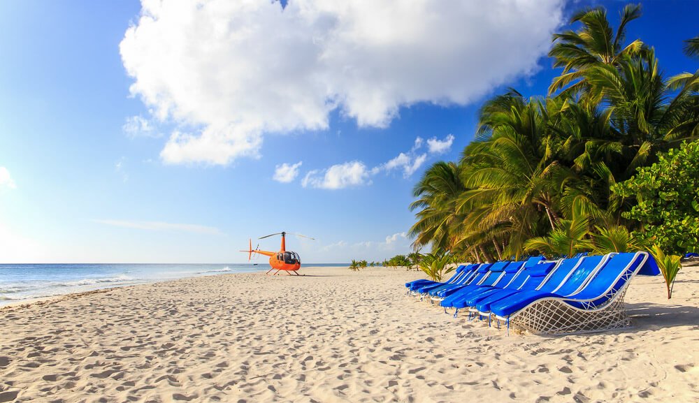 Helicóptero laranja, pousado em praia de areia clara, na República Dominicana.