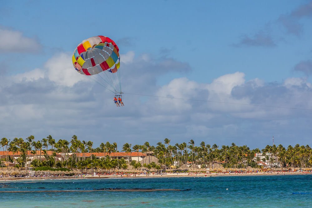 Duas pessoas com colete laranja sobrevoam o mar de Punta Cana, em um parasailing colorido