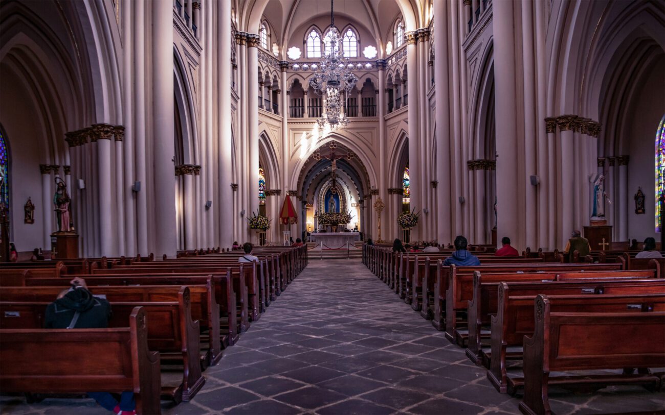 Bancos de madeira com alguns fiéis observando o altar da Basílica Menor Nuestra Señora de Lourdes, na Zona G, em Bogotá.